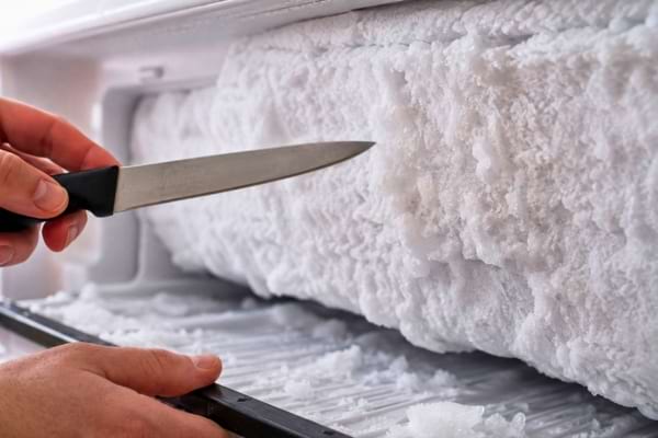 une personne tenant un couteau pour enlever du givre d'un congélateur
