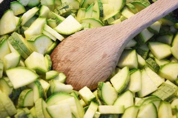des courgettes coupées en morceaux dans une poêle avec une cuillère en bois