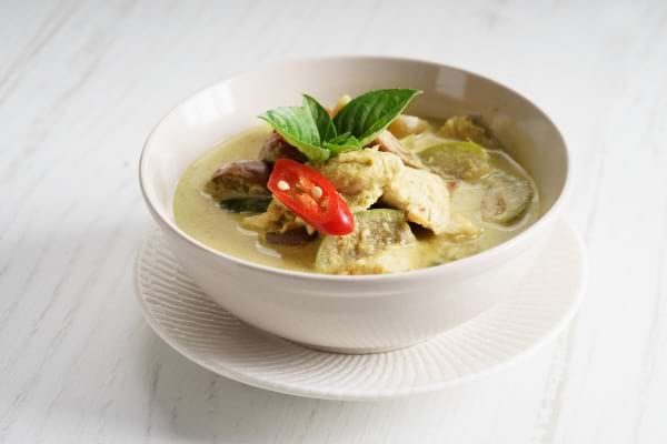 un curry de courgettes au lait de coco avec piment présenté dans une assiette blanche creuse