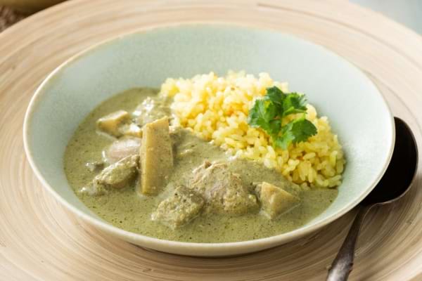 une assiette blanche creuse avec un curry au lait coco végétarien des courgettes et du riz