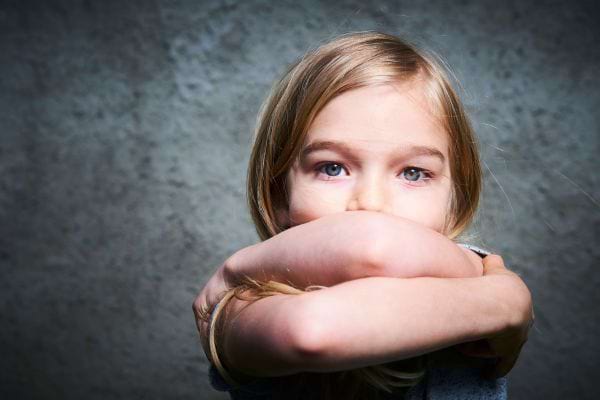 une enfant blonde les yeux bleus croise les bras dans un geste protecteur