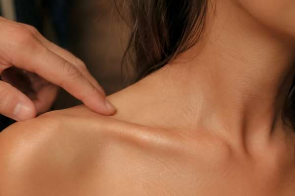 fingertips gently tracing along a woman's collarbone, soft warm lighting