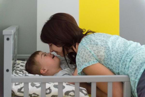 une jeune femme brune se penche sur un enfant trisomique dans son lit pour lui faire un bisou