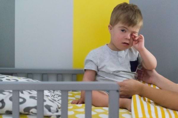 des bras se tendent vers un enfant atteint de trisomie assis dans son lit