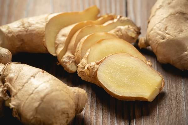 Racines de gingembre frais, dont une coupée en plusieurs tranches.