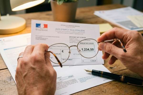 mains tenant des lunettes de lecture posées sur un avis d'imposition français imprimé