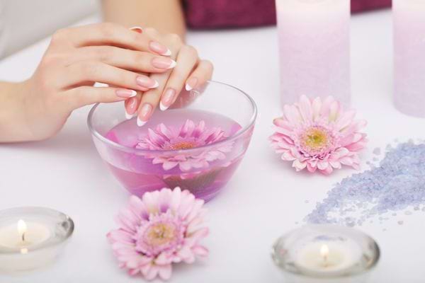 des mains manucurés au-dessus d'un bol avec des fleurs pour faire un soin