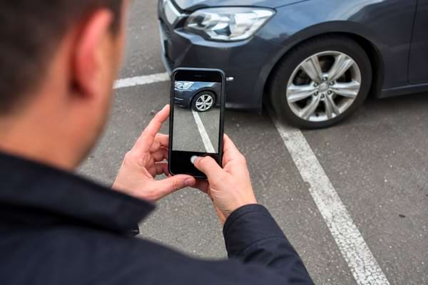 ne personne tenant un smartphone pour prendre en photo la roue de sa voiture mal garée sur un parking