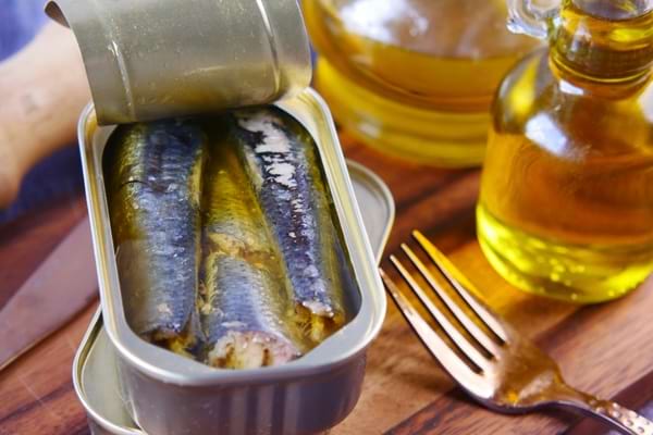 Sardines en boîte servies avec de l’huile d’olive sur une table en bois.