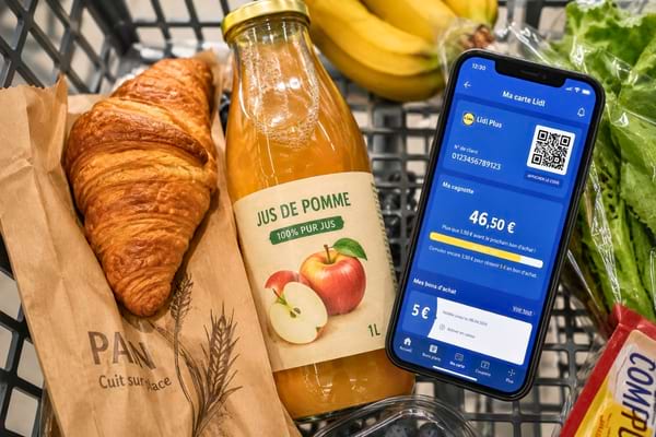 Un croissant doré et croustillant posé à côté d'une bouteille de jus de pomme et d'un smartphone