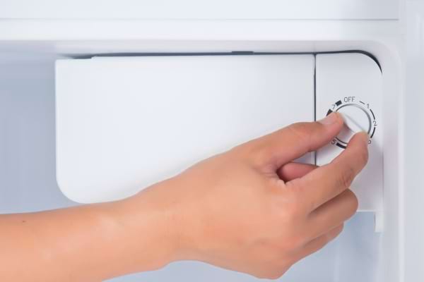 Une main qui règle le thermostat d'un frigo