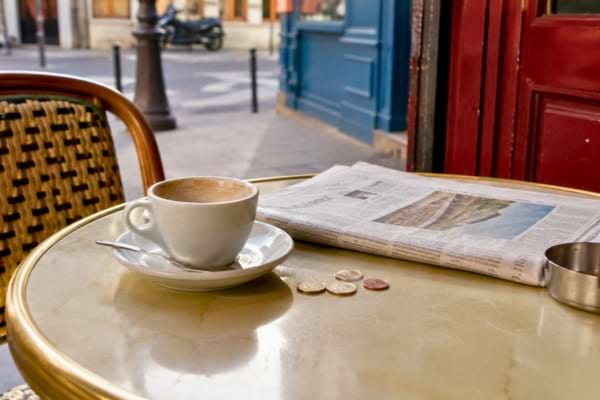 une table de bistrot parisien typique avec une tasse de café vide, un journal et quelques pièces