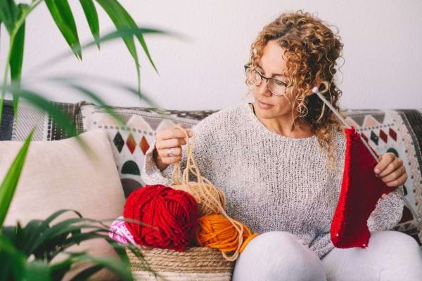 une femme dans son canap&eacute; choisit une pelote et tricote avec de la laine rouge