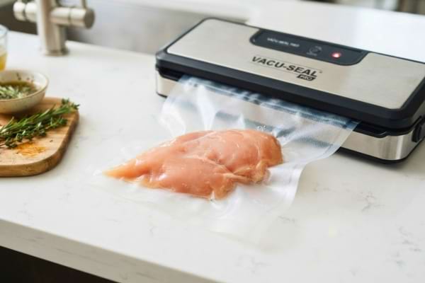 Close up of raw chicken breasts being vacuum-sealed in clear plastic