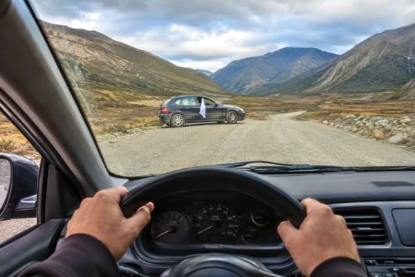 une voiture montrant les mains du conducteur sur le volant qui ralentit prudemment en voyant au loin un v&eacute;hicule arr&ecirc;t&eacute;