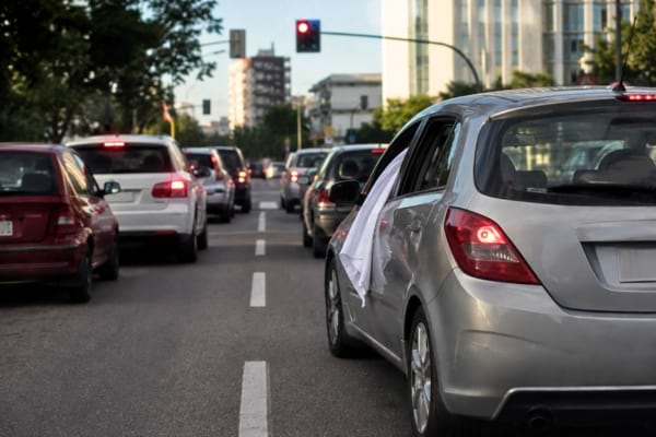 une route urbaine avec un feu rouge, une voiture avec un tissu blanc &agrave; la fen&ecirc;tre attend patiemment
