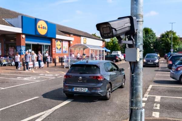 a modern security camera mounted on a metal pole at the entrance of a supermarket parking lot