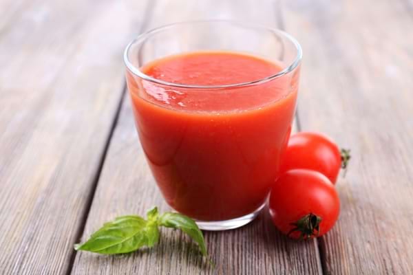 Verre de jus de tomate maison accompagné de tomates fraîches et de feuilles de basilic.