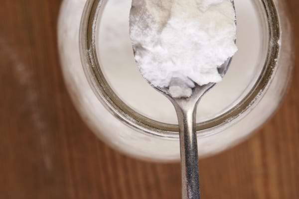 Cuillère remplie d'une poudre blanche au-dessus d’un bocal en verre.