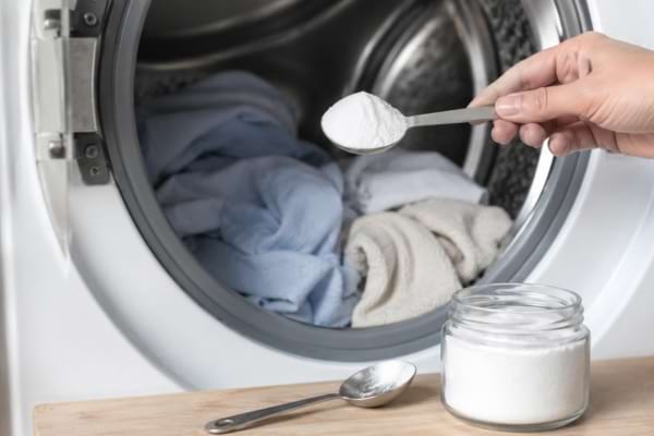 Bicarbonate de soude devant une machine à laver et un panier de linge propre.