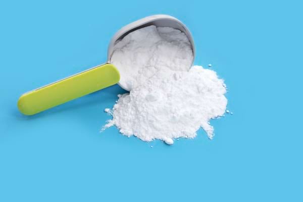 Bicarbonate de soude renversé sur un fond bleu avec une cuillère doseuse verte.