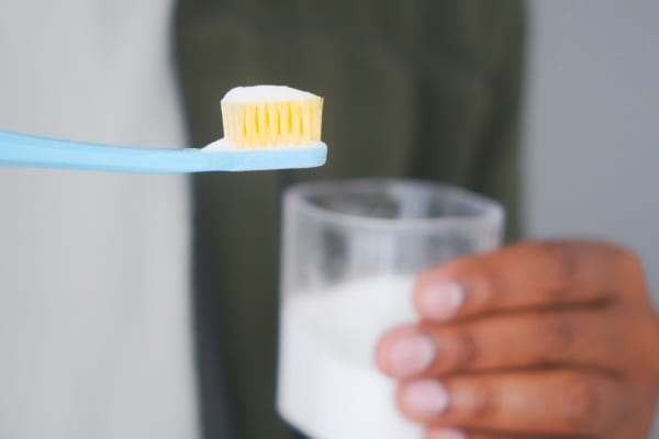 Brosse à dents recouverte de bicarbonate devant un verre d’eau.