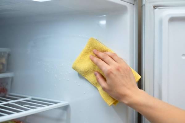 Une main passant un chiffon en microfibre jaune propre sur la paroi intérieure d'un congélateur
