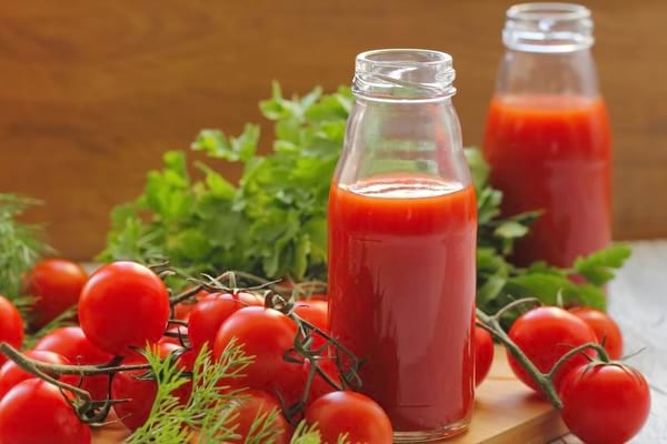 Bouteilles de jus de tomate maison entourées de tomates fraîches et d’herbes aromatiques.