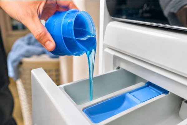 un bouchon doseur rempli de lessive liquide versé au-dessus du tiroir d'une machine à laver