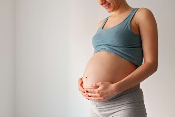 Femme enceinte souriante tenant délicatement son ventre.