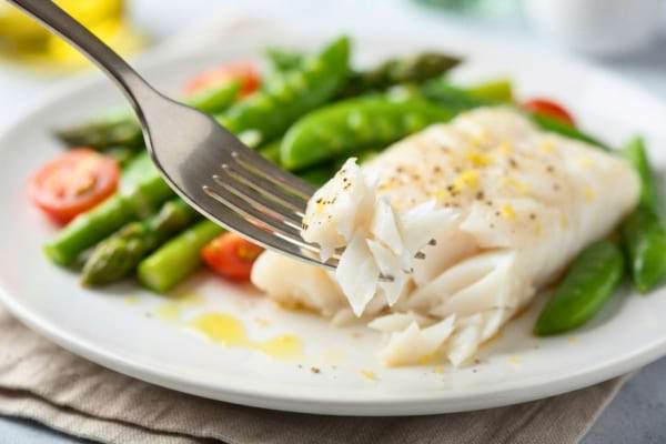 'une fourchette piquant un morceau de poisson blanc cuit à la perfection