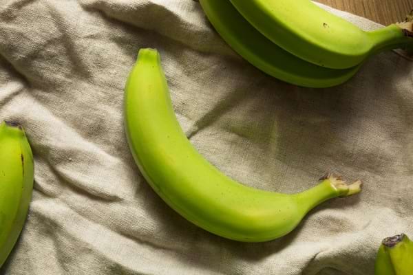 Bananes vertes posées sur un tissu beige.