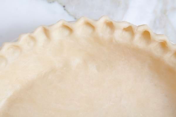 Pâte à tarte maison crue étalée dans un moule avec des bords soigneusement façonnés.