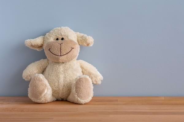 Peluche en forme de mouton assise devant un mur bleu.