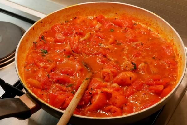 Tomates mijotées avec des herbes dans une poêle, remuées avec une cuillère en bois.