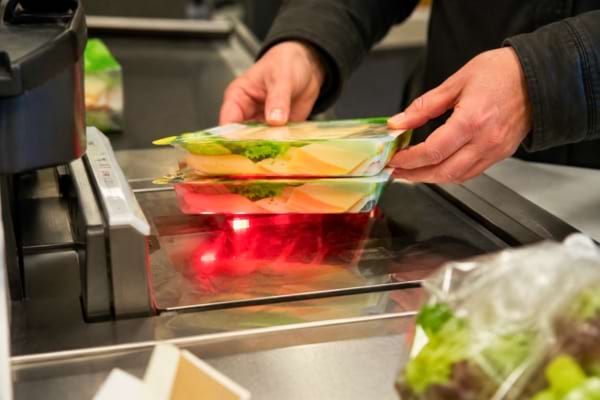 'un client à une caisse automatique de supermarché, empilant discrètement deux articles identiques au-dessus du scanne