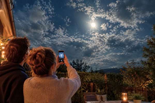 deux personnes qui prennent en photo la lune dans les nuages