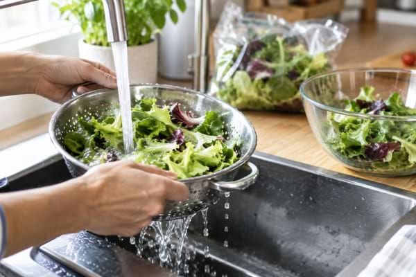 Salade en sachet rincée sous l’eau froide dans une passoire avant le repas.