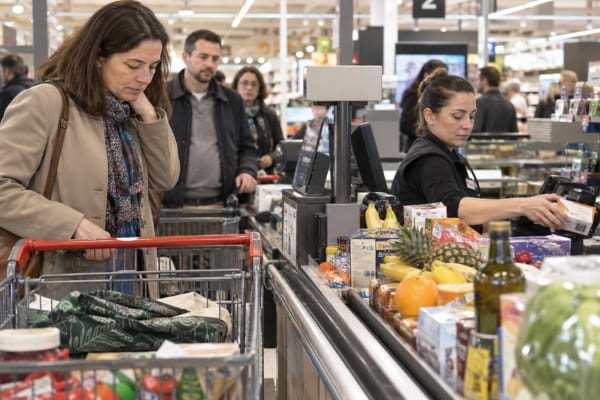 Cliente à la caisse avec ses sacs encore pliés pendant que les courses s’accumulent sur le tapis.