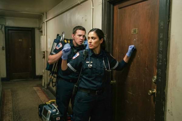 Paramedics standing outside a closed residential door, looking urgent