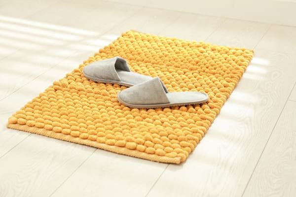 Paire de chaussons gris posée sur un tapis de bain jaune.