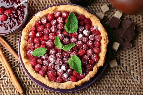 arte aux framboises décorée de menthe et de sucre glace, accompagnée de chocolat.