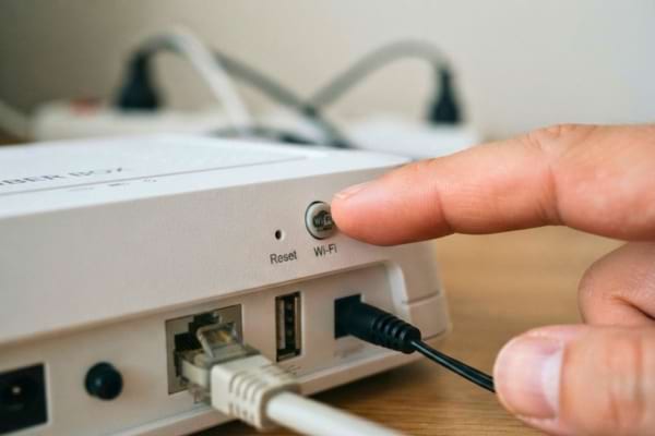 un doigt s'apprêtant à appuyer sur le bouton "Wi-Fi" situé à l'arrière d'un boîtier internet blanc