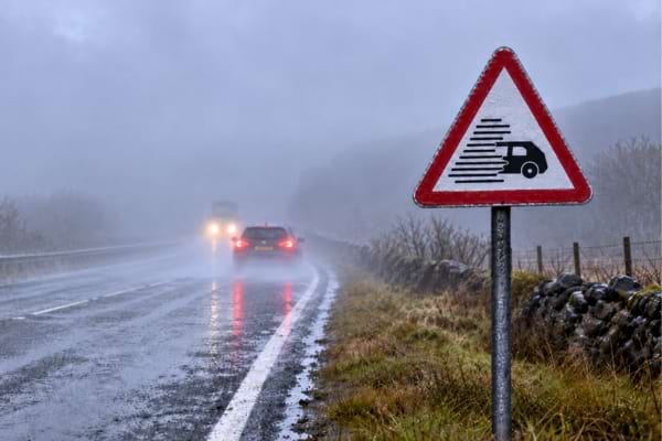 Un panneau P33 sur une route avec peu de visibilité à cause de la pluie et brouillard