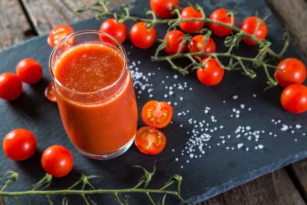 Verre de jus de tomate servi avec des tomates cerises et quelques grains de sel.