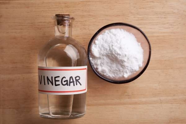 Bouteille de vinaigre et bol de bicarbonate de soude sur une table en bois.