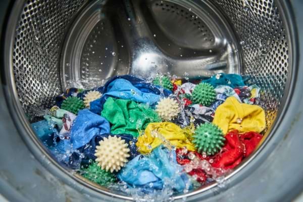 intérieur d'un tambour de machine à laver en acier inoxydable, avec des vêtements colorés et des balles de lavage en action