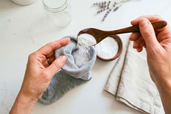 he person is pouring white baking soda powder from a wooden spoon into the open sock