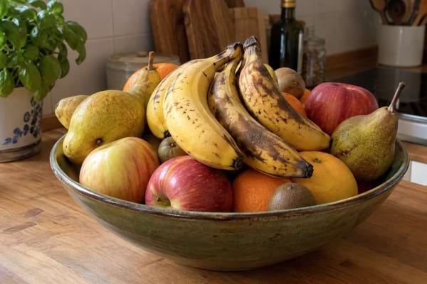 Corbeille de fruits remplie de bananes, pommes, poires et agrumes dans une cuisine