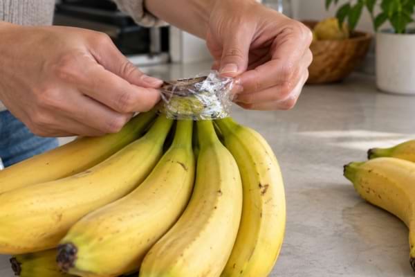 1. Mains enveloppant la tige d’un régime de bananes avec du film alimentaire